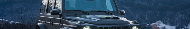 Black Mercedes-Benz G-Class SUV on a mountain road with snow-covered trees and mountains in the background.