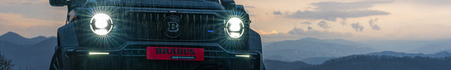 SUV with headlights on against a mountainous landscape during sunset.
