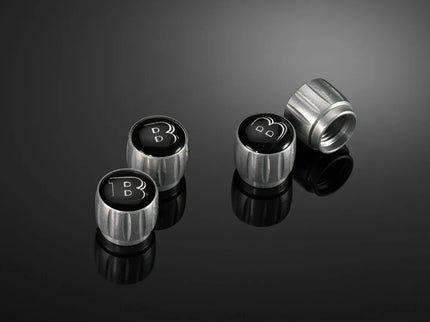 Four metallic valve stem caps with a logo on a reflective black surface