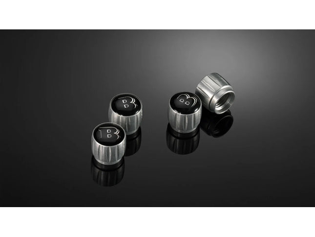 Four metallic valve stem caps with a logo on a reflective black surface