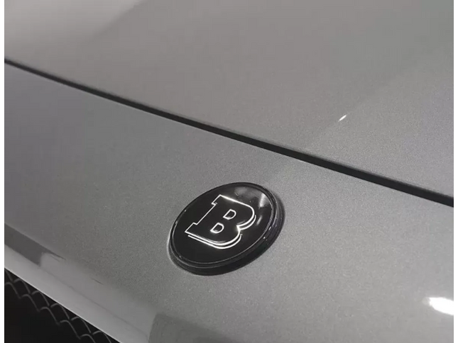 Close-up of a car emblem with a letter 'B' on a gray vehicle surface.