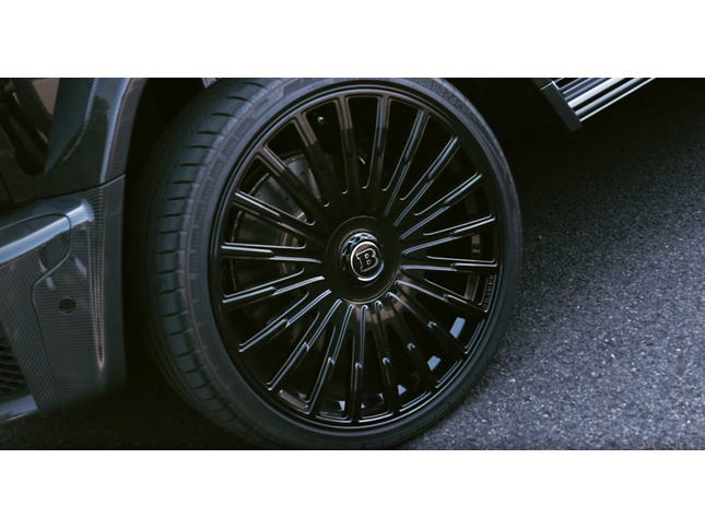 Close-up of a car wheel with a detailed rim design on a dark surface.
