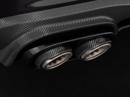 Close-up of a car's carbon fiber exhaust system with a prominent brand logo on a dark background.